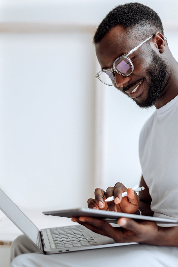 A smiling man using a tablet and laptop in a bright indoor setting. Perfect for technology and lifestyle themes.